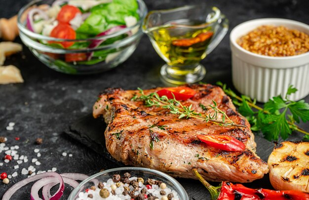 Bbq grilled pork steak with spices and vegetables on dark background