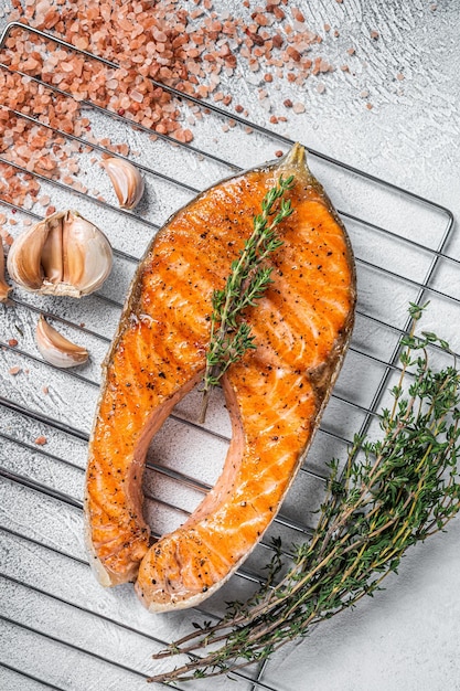 BBQ grilled Salmon Fish Steak on a grill with thyme and pink salt. White background. Top view