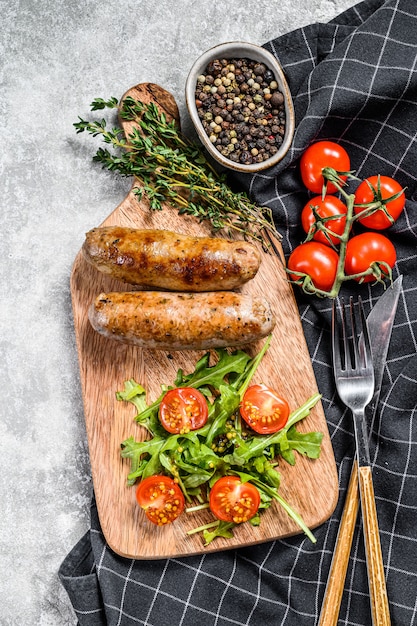 BBQ Grilled sausages on a chopping Board with tomato and arugula.