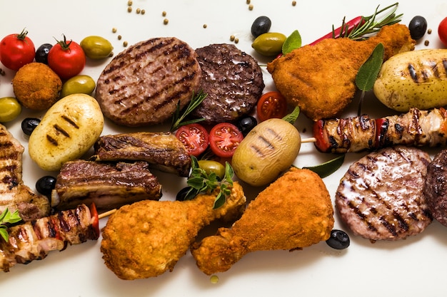 Festa con carne alla griglia con diversi tipi di carne: hamburger di manzo, costolette di maiale, polpette di tacchino, cosce di pollo impanate con patate e pomodori, spezie ed erbe aromatiche. menu estivo