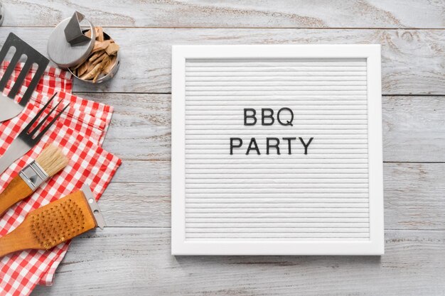 Знак BBQ Party с инструментами для приготовления барбекю на деревянном фоне.