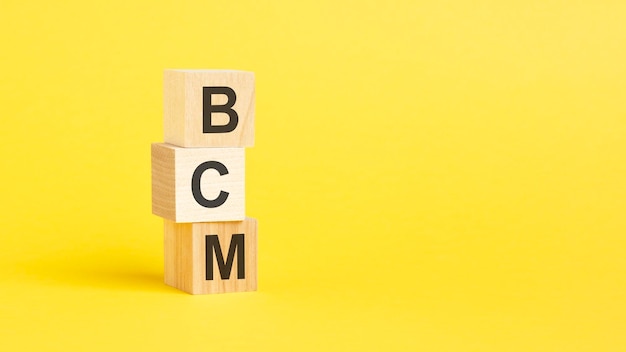 BCM text on wooden cubes on yellow background