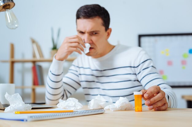 Do not be afraid. Serious male person wiping his nose and putting elbows on the table while looking forward