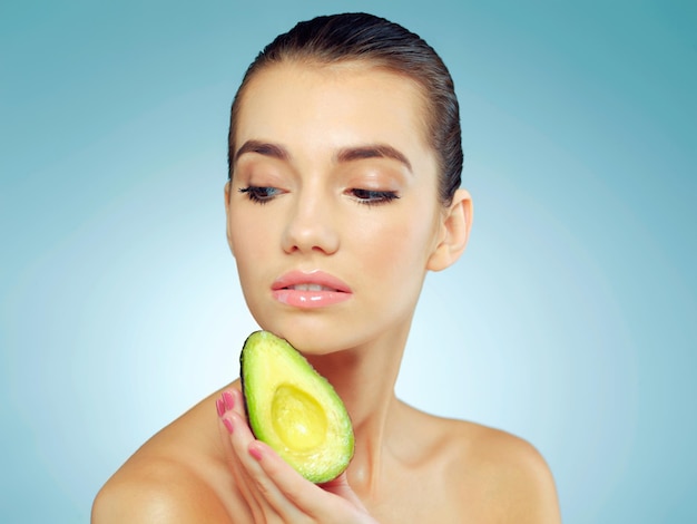 Be nice to your skin and feed it natural oils Studio shot of a beautiful young woman holding an avocado against a blue background