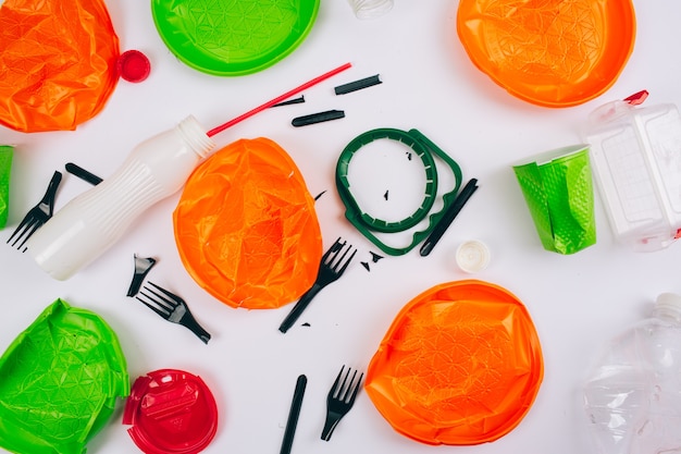 Be plastic free. Save ecology. Broken single-use colorful plastic items on white background.