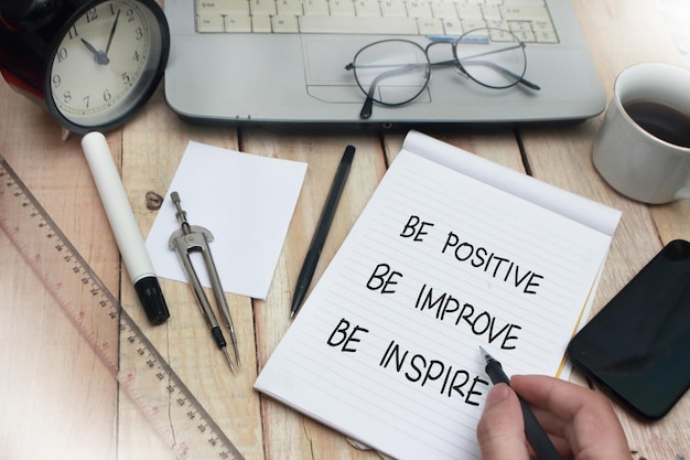 Photo be positive improve inspire words letter written on notepad work desk top view