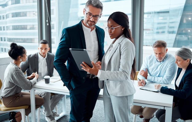 Sii intelligente con i tuoi processi aziendali inquadratura di due uomini d'affari che utilizzano una tavoletta digitale in un ufficio con i colleghi in background