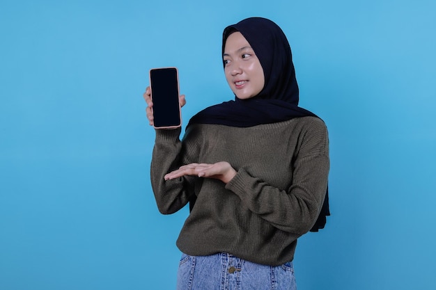 Be smart buy this device, portrait of young asian woman laughing out loud, wearing hijab pointing at smartphone, showing device screen