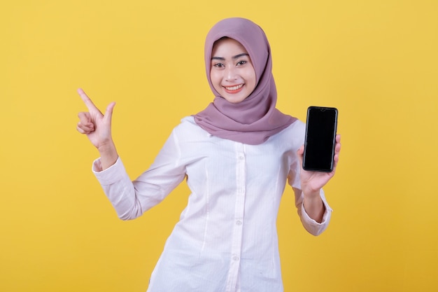 Be smart buy this device, portrait of young asian woman laughing out loud, wearing hijab pointing at upper, showing device screen