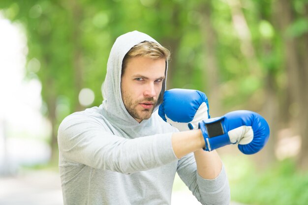 Be strong. man in boxing gloves punching. Sport and sportswear fashion. boxer man in hood. ready to fight. knockout and energy. Sport success. Boxing school. training with coach. healthy fitness.