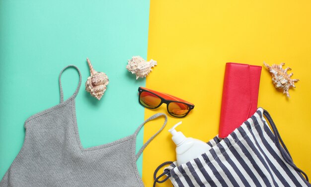 Beach accessories on a colored pastel background. Beach bag, T-shirt, sunglasses, purse, sunblock, cockleshells. Top View