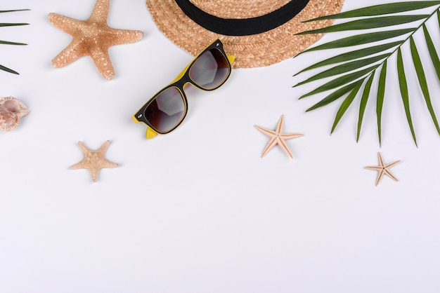 Beach accessories: glasses and hat with shells and sea stars on a white background. Summer background