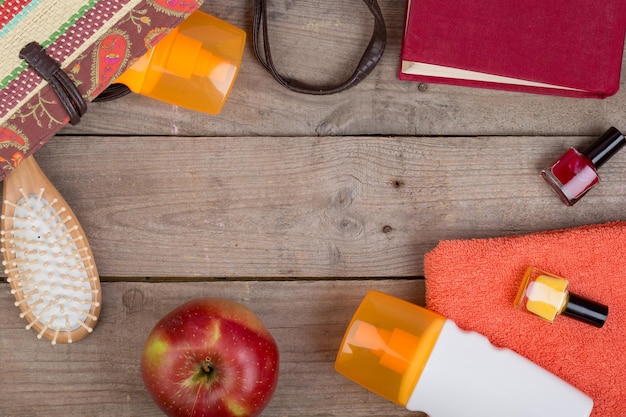 Beach accessories hairbrush orange towel sun cream lotion beach bag nail polish a book on a brown wooden background