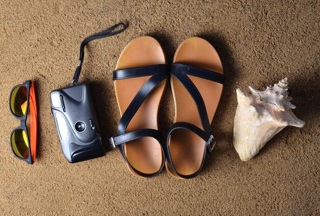 Beach accessories lie on the sand.Camera, sandals, sunglasses, seashells.  The concept of relaxing at sea. Summer beach season is open! Top view.