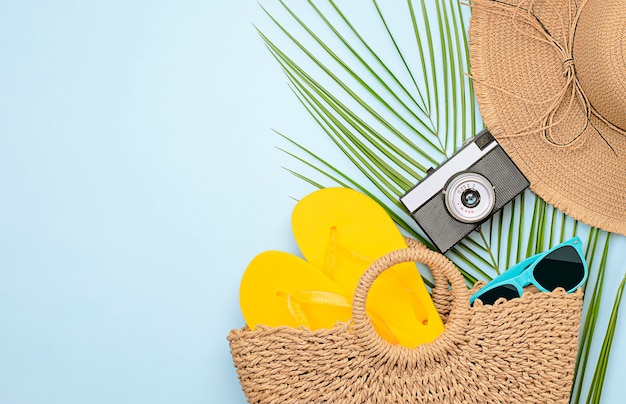 Beach bag, flip flops, sunglasses, sun hat, camera and palm leaf on light blue background