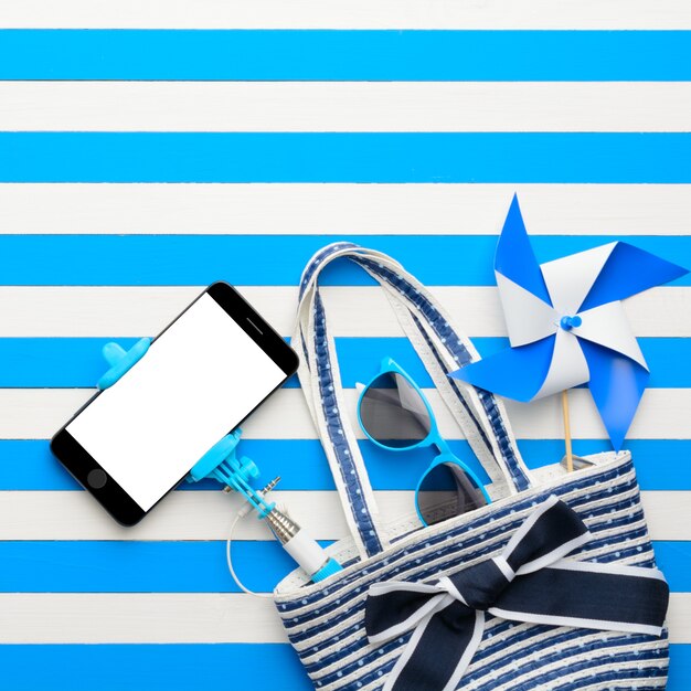 白と青の背景にビーチバッグ、サングラス、スマートフォン。上面図、フラットレイ。
