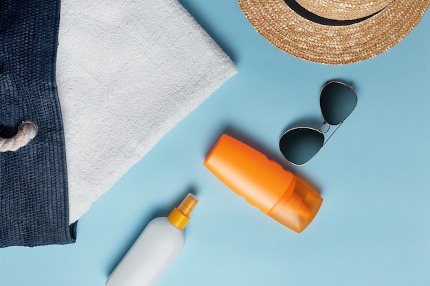 Borsa da spiaggia con accessori da spiaggia su uno sfondo colorato vista dall'alto. crema solare, asciugamano, occhiali, cappello.