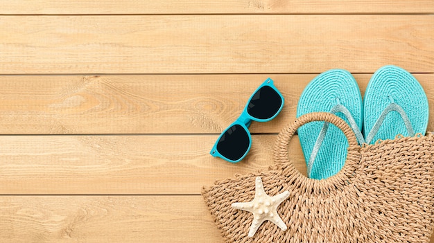 Beach bag with sunglasses and flip flops on wooden background