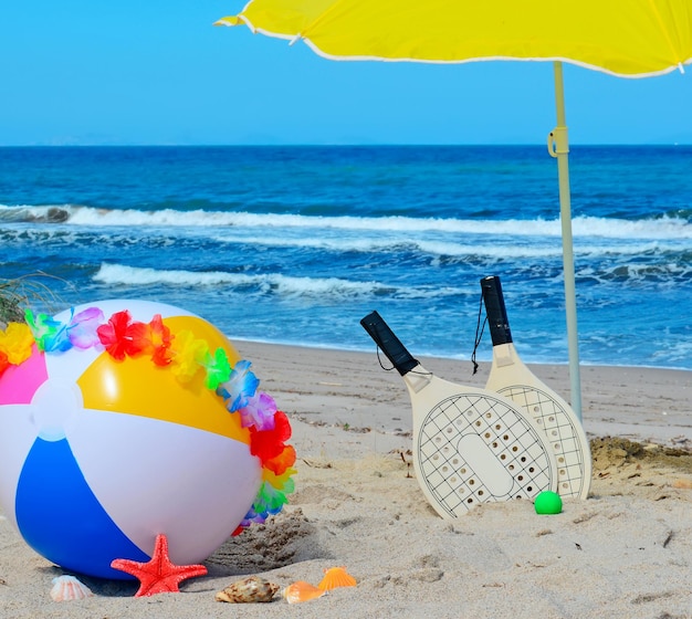 Beach ball with necklace rackets and parasol by the sea