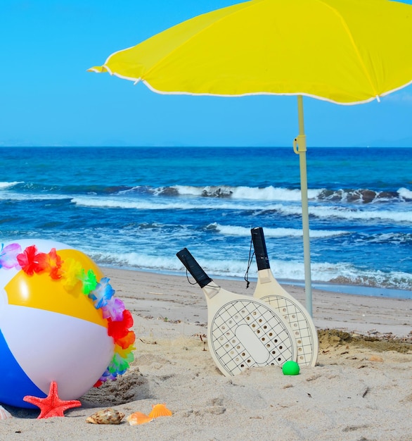 Beach ball with necklace rackets and parasol by the sea