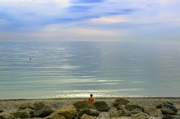 흑해 연안의 해변 바위 사이에서 한 남자가 바다를 바라보고 있다 Adler Sochi Russia 2021