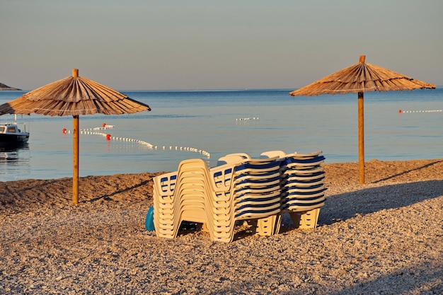 Фото Пляжные стулья и зонтики на галечном пляже во время восхода солнца