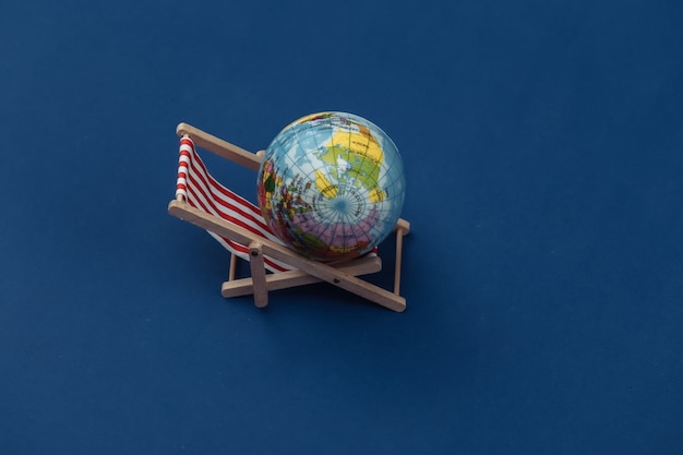 Photo beach deck chair with globe on classic blue background. color 2020.