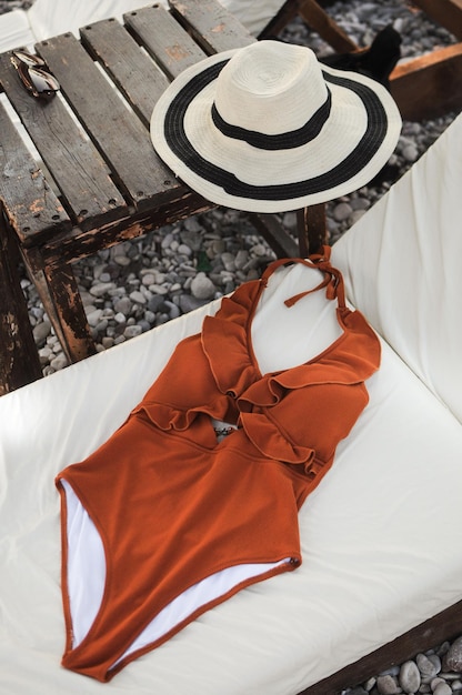 Beach female accessories straw hat and swimsuit on sunbed on the pebble beach