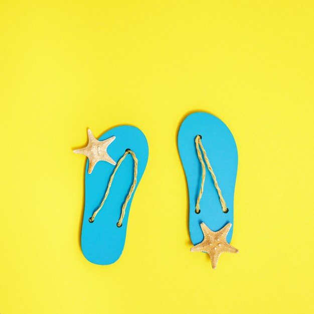 Beach flip-flops and small starfishes on bright yellow paper