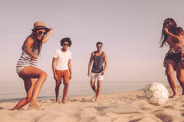 Пляжное развлечение. Группа веселых молодых людей, играющих с футбольным мячом на пляже