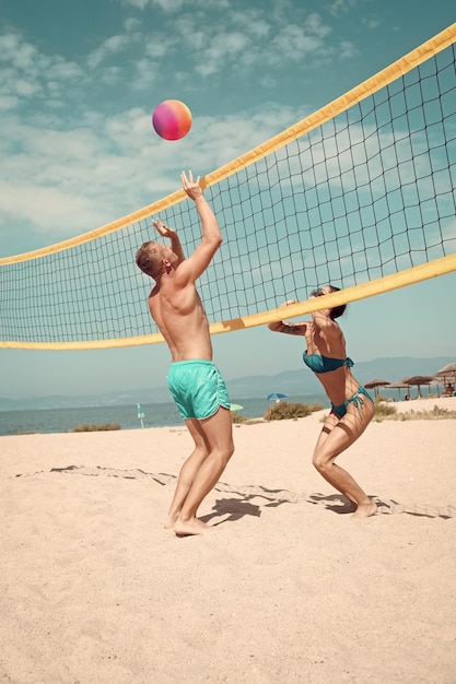 Beach games beach volleyball concept couple have fun playing\
volleyball young sporty active couple beat off volley ball play\
game on summer day woman and man fit strong healthy doing sport on\
beach