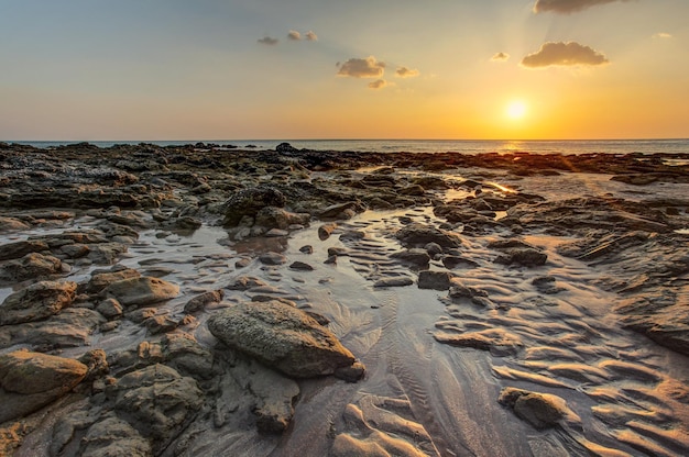 干潮時の金色の夕焼けのビーチは、海に覆われていない砂の層と湿った石を示しています。カンティアン湾、ランタ島、タイ。