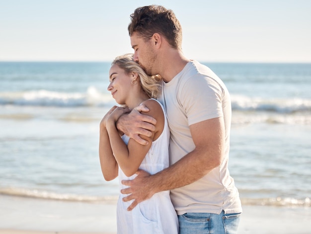 Beach happy and couple hugging with love care and romance while on a honeymoon vacation Happiness kiss and loving man embracing his wife from behind by the ocean on a seaside holiday in Maldives