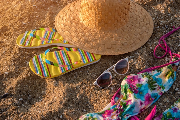 Cappello da spiaggia e occhiali da sole infradito sdraiati sulla sabbia lasciano problemi e trambusto dietro il caldo resort tropicale