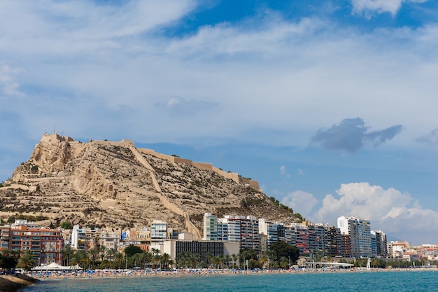 Beach line in city of Alicante with Castle of Santa Barbara in the background.