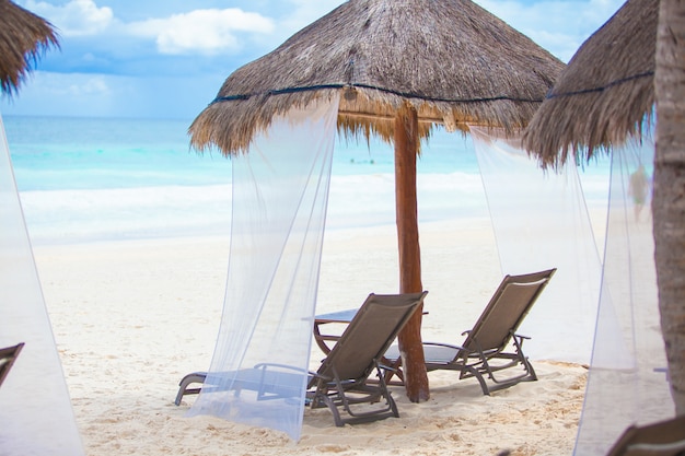 Beach loungers under thatched umbrellas on tropical plage