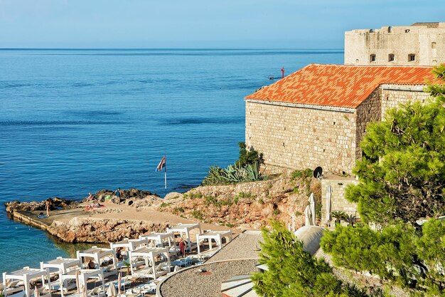 크로아티아 두브로브니크(Dubrovnik)의 아드리아 해(Adriatic Sea)에 있는 해변과 오래된 요새. 배경에 사람들