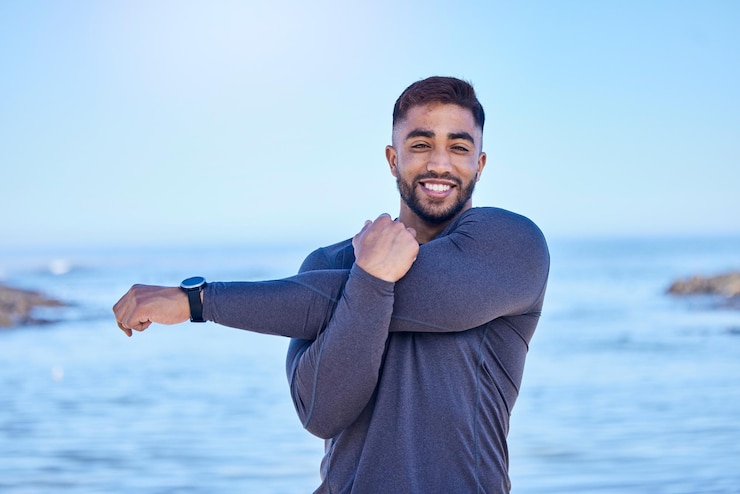 Photo beach portrait exercise and happy man stretching arm for outdoor freedom sports workout or start routine blue sky natural sea water and indian person doing relax training warm up on nature island