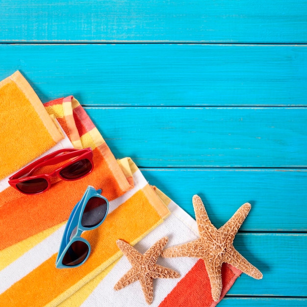 Photo beach scene with orange striped towel, starfish and sunglasses on old blue painted wood decking.  space for copy.