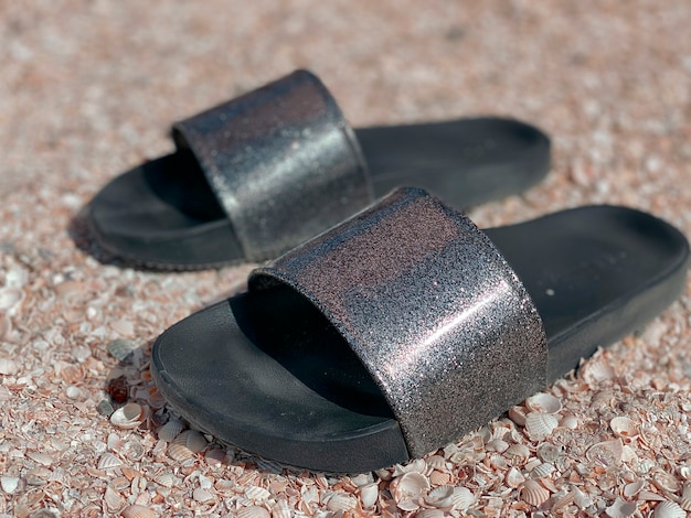 Beach slippers with black soles and shimmery silver upper stand close-up on a pebble beach.