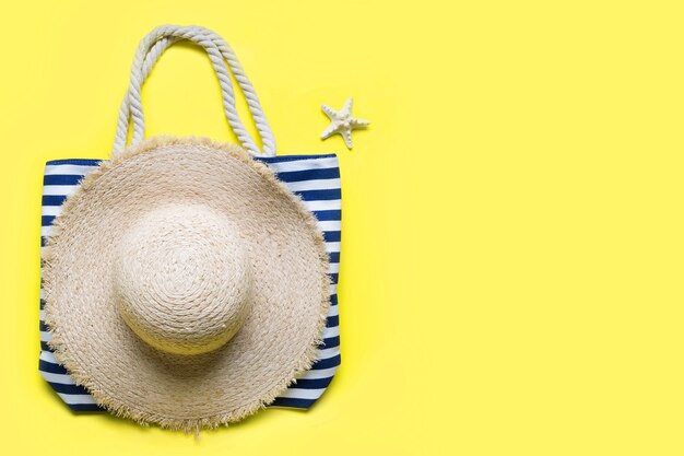 Beach striped bag straw sunhat and seashell on yellow background