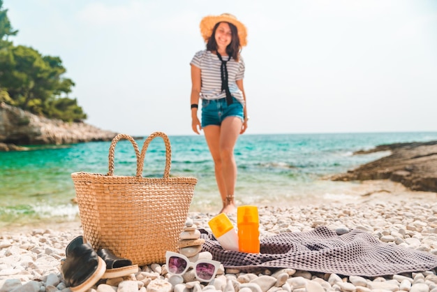 Beach stuff straw hat and bag with flippers and sun protection cream at seashore woman on background