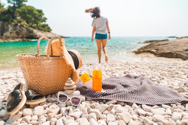 Beach stuff straw hat and bag with flippers and sun protection cream at seashore woman on background
