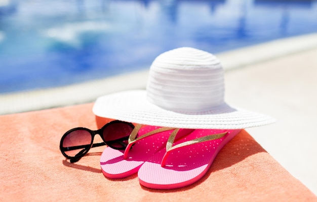 beach, summer, vacation and accessories concept - close up of hat, flip-flops and sunglasses at pool