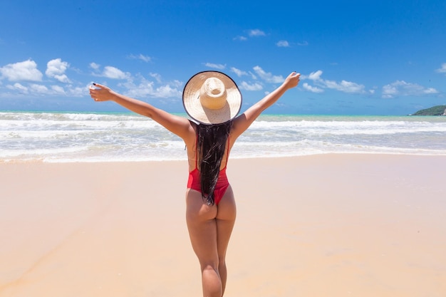 Donna per le vacanze estive in spiaggia nel concetto di libertà felice con le braccia alzate nella felicità modello di donna che indossa un costume da bagno rosso e un cappello da spiaggia