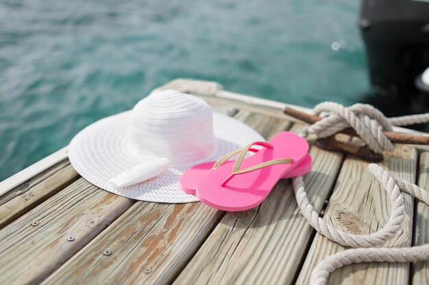 beach, summer, vacations and accessories concept - close up of hat, sunscreen and slippers at seaside