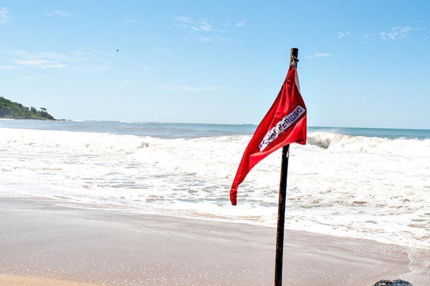 Beach on sunny day with red flag written dangerous place in Portuguese
