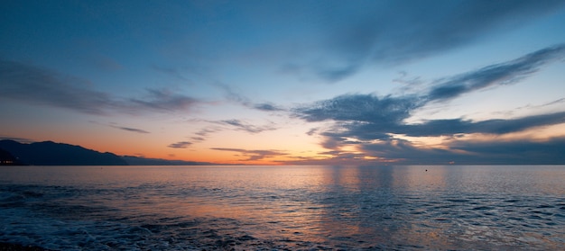 Tramonto sulla spiaggia con orizzonte infinito e onde calme sulle montagne in lontananza