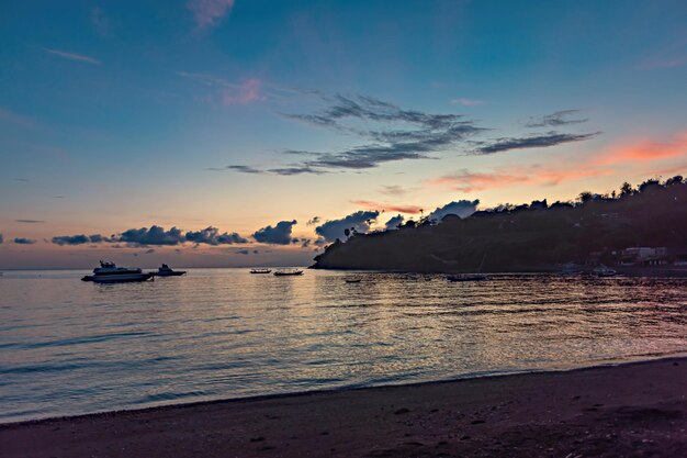 A beach at sunset with a few boats in the water