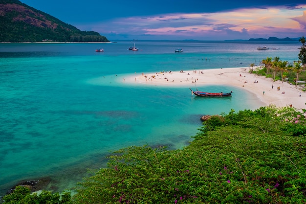 Beach that extends into the sea Looking out to see the island And blue sky There are many boats floating in the emerald green sea of the Andaman Sea.